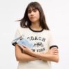 Håndleddsveske med glidelås i hjørnet i «Loved Denim» med anheng